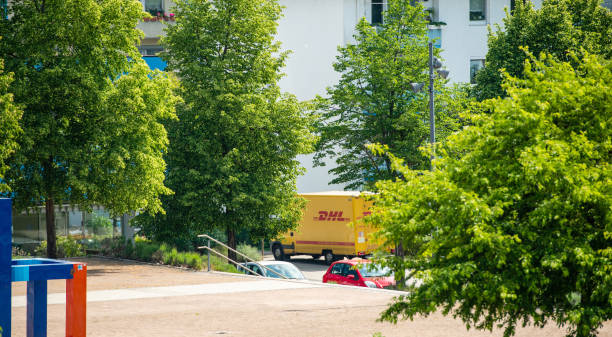 view through trees of  yellow dhl van driving street - driving delivery van global business dhl imagens e fotografias de stock