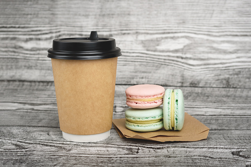 A cup of coffee to go and delicious macaron near it on the grey wooden background.