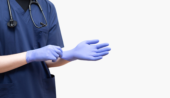 A doctor in a blue uniform putting on sterile gloves on a white background. Banner. Coronavirus, covid-19, healthcare concept.