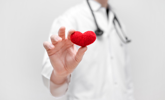 The doctor holds a red heart in his hands on a white background. Coronavirus, covid-19, healthcare concept. Cardiology.