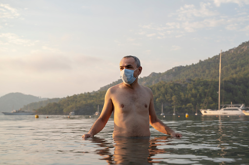 Mature man swimming in the sea with a surgical mask during Covid-19 pandemic