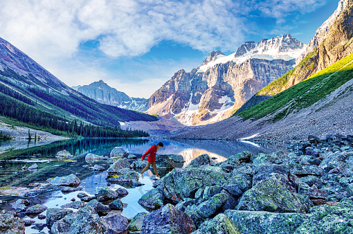 Teenage boy hiker rock hopping across Consolation Lake near Lake Louise in Banff National Park, Alberta, Canada, with Mount Quadra in the background.