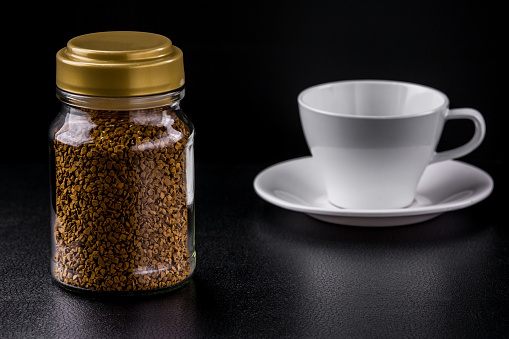 Glass bottle instant coffee and empty white cup on black background