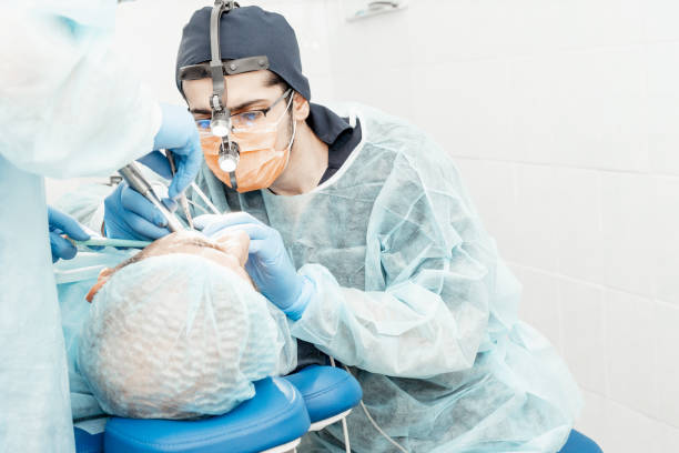 istock Patient and dentist during implant placement operation. Real operation. Tooth extraction, implants. Professional uniform and equipment of a dentist. Healthcare Equipping a doctorâs workplace. Dentistry 1263965456