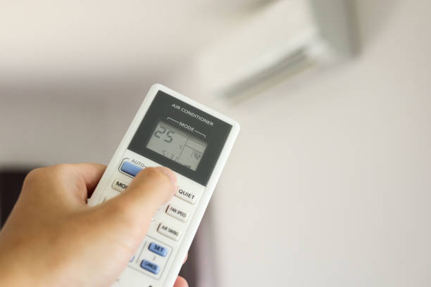 istock Hand with remote control directed on air conditioner inside the room 1263965813