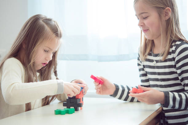Two Young Schoolgirls Playing with Colorful Puzzle Cube During School Break stock photo