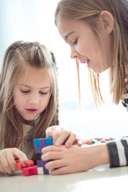 istock Two Young Schoolgirls Playing with Colorful Puzzle Cube During School Break 1263966144