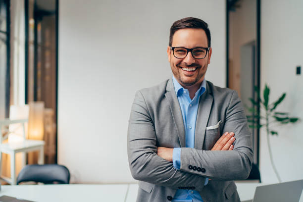 Portrait of young businessman standing in his office with arms crossed Portrait of young happy businessman wearing grey suit and blue shirt standing in his office and smiling with arms crossed director photos stock pictures, royalty-free photos & images
