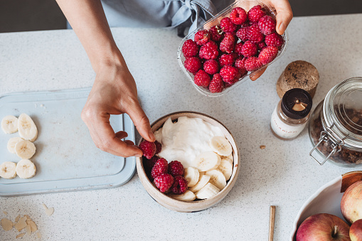Healthy breakfast: anonymous woman making oatmeal with Greek yoghurt, raspberries, strawberries and a banana, a close up.