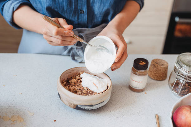 Hands of a Woman Adding Greek Yoghurt to Rolled Oats, Healthy Breakfast Concept Making breakfast: unrecognizable woman adding yoghurt to oatmeal. greek yogurt photos stock pictures, royalty-free photos & images