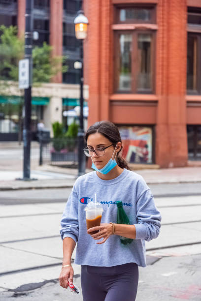 A girl walking. A girl walking downtown Toronto while waring a mask and holding a drink. She is holding the drink after coming out of a cafe. flatiron building toronto stock pictures, royalty-free photos & images