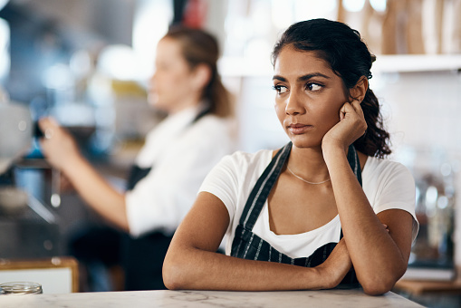 Shot of a young woman looking unhappy while working behind the counter of a cafe