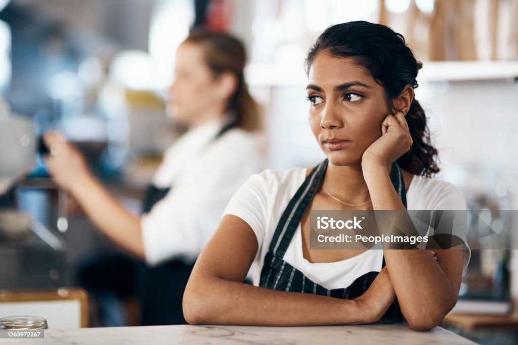 Could a change in career be on the menu? Shot of a young woman looking unhappy while working behind the counter of a cafe Occupation Stock Photo