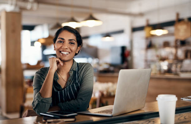 Nothing empowers you more than owning your own small business Shot of a young woman using a laptop while working in a cafe apron photos stock pictures, royalty-free photos & images