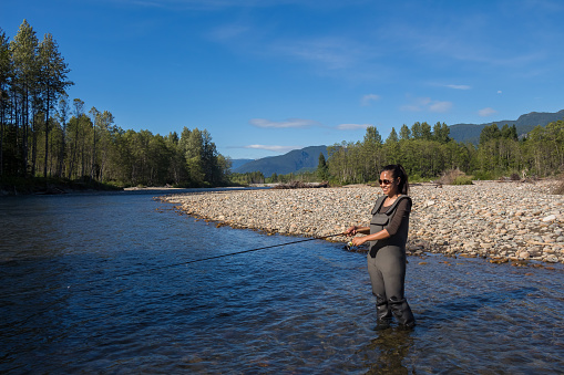 An asian women in waders, enjoying fishing the Kitimat River, Skeena Region, in British Columbia, Canada