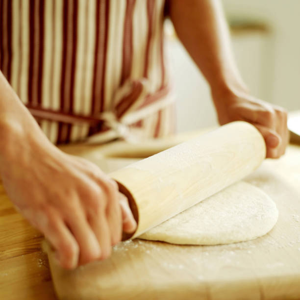 istock Chef rolling out pizza dough with a wooden rolling pin wearing a red stripy apron 1263980647