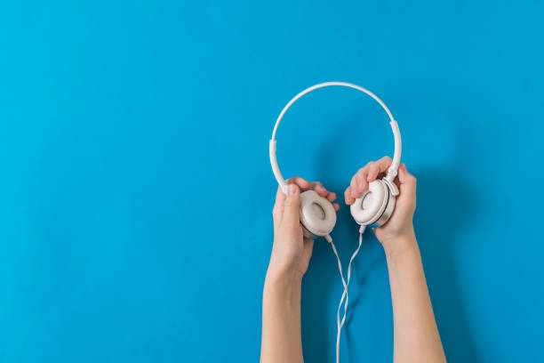 istock Two hands holding white headphones on a blue background. 1263983033