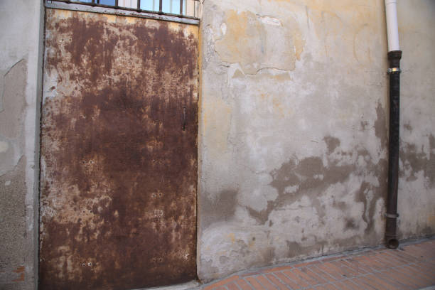istock Rusty metal door in a worn white wall 1263985511