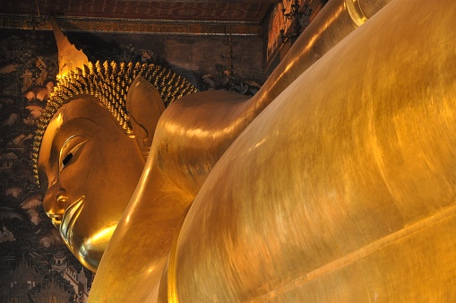The Recling Buddha of Wat Pho, also knwon as Temple of the Reclining Buddha, in Bangkok, Thailand. The posture of the image is referred to as sihasaiyas, the posture of a sleeping or reclining lion. The figure is 15 m high and 46 m long, and it is one of the largest Buddha statues in Thailand. The figure has a brick core, which was modelled and shaped with plaster, then gilded.