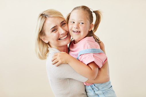 Portrait of happy mother embracing her daughter with down syndrome against the white background