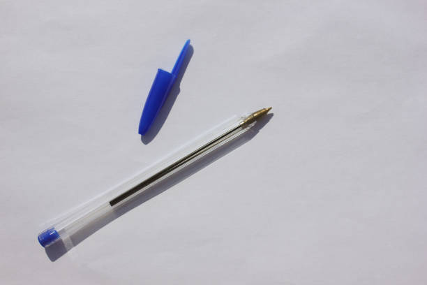 A close-up macro shot of a ballpoint pen tip resting on a stack of white paper. The image captures the precision of the pen and the texture of the paper, emphasizing detail, craftsmanship, and writing instruments