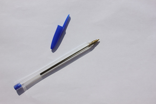 Single ballpoint pen with a letter cap on a brown background. View from above. The case handles white, caps blue. Education. Schooling. For work. Flatlay. Copy spase for text