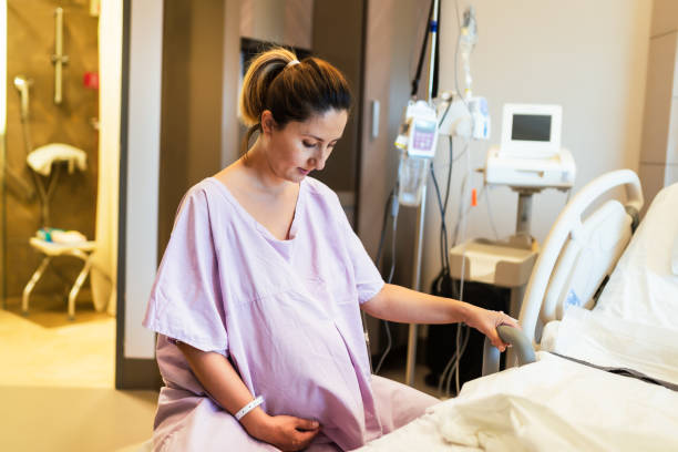 jovem grávida na ala hospitalar sentada na bola fitness e pronta para o parto de um bebê. - delivery room - fotografias e filmes do acervo