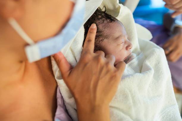 Mother holding her newborn baby for the first time in delivery room during covid-19 Mother holding her newborn baby for the first time in delivery room during covid-19 labor childbirth photos stock pictures, royalty-free photos & images