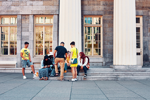 Montreal, Canada - June, 2018: Group of diverse young students sitting and having a joyful conversation on the exterior stairs of Marche Bonsecours in Montreal, Quebec, Canada.