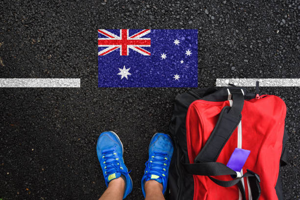 a man with a shoes and travel bag is standing on asphalt next to flag of Australia and border stock photo