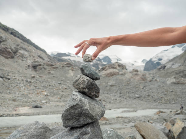 View of hand stacking rocks on mountain trail, glacier view