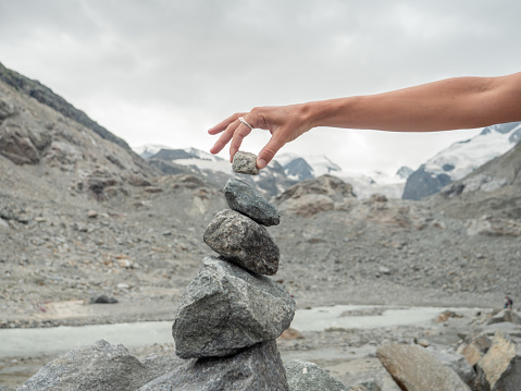 Female's hand stacking rocks against glacier view in Switzerland