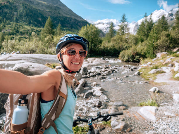 istock Young woman mountain biker on trail takes selfie 1264025061