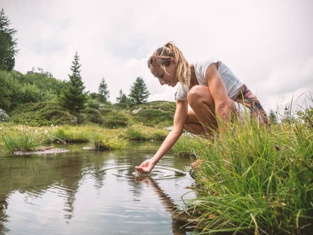 woman capturing fresh water from alpine lake - mountain drop europe switzerland imagens e fotografias de stock