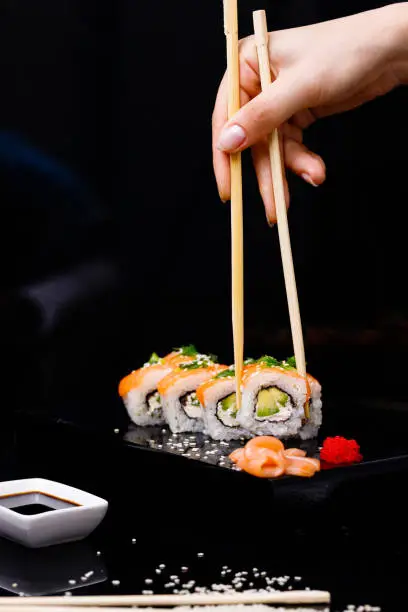 Photo of Sushi with salmon. Soy sauce, red caviar. Sushi on a black background.