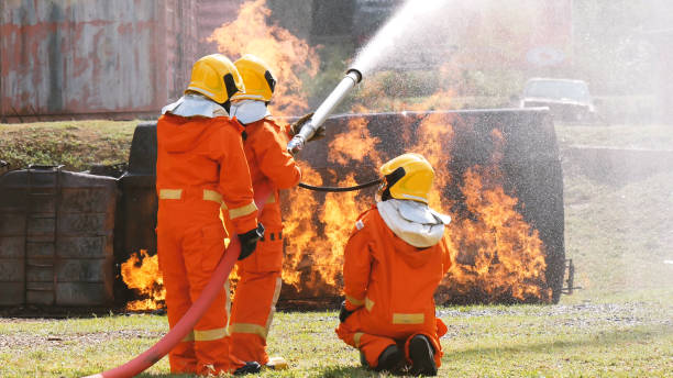 istock Firefighter fighting with flame using fire hose chemical water foam spray engine. Fireman wear hard hat, body safe suit uniform for protection. Rescue training in fire fighting extinguisher 1264042126