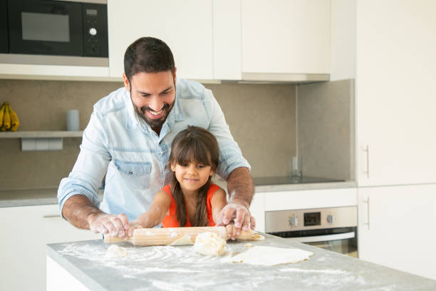 istock Cheerful Latin girl and her dad rolling and kneading dough 1264044693