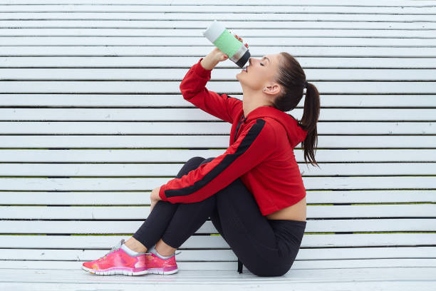 istock Attractive girl in sportswear, during a break, drinks water on a white bench 1264044779