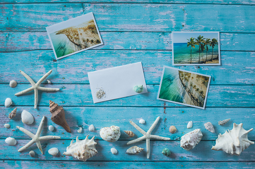 Directly above shot of ocean themed background with arrangements of seashells, starfish and tropical postcards against a sea blue wooden table underneath.