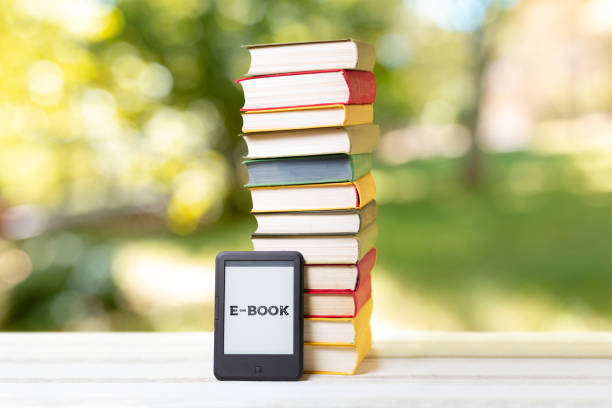 istock Reading. E-book reader and a stack of books. The park is blurred in the background. Concept of education and electronic gadgets 1264046377