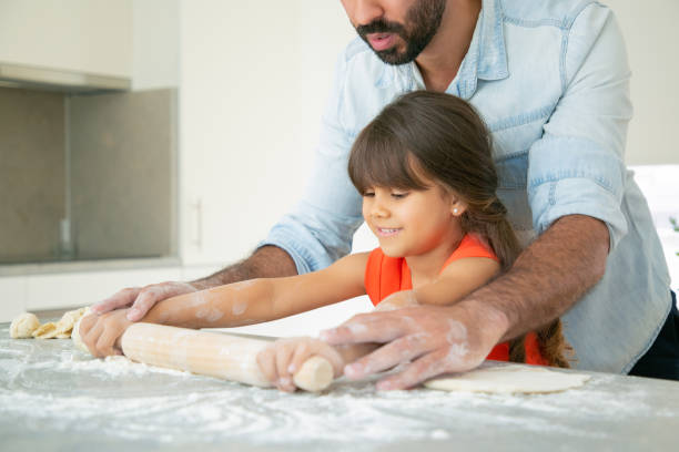istock Happy girl and her dad rolling dough on kitchen table 1264047783