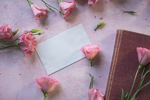 Love letter. white card with pink paper envelope mock up. Petals of flowers, roses and ranunculus. Valentine's day romantic background . High quality photo