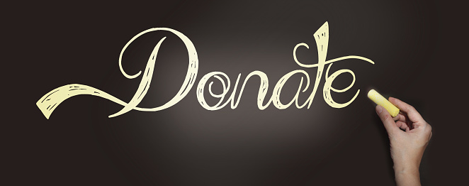 Hand writing the word Donate with chalk on blackboard. Donation help volunteers support concept.