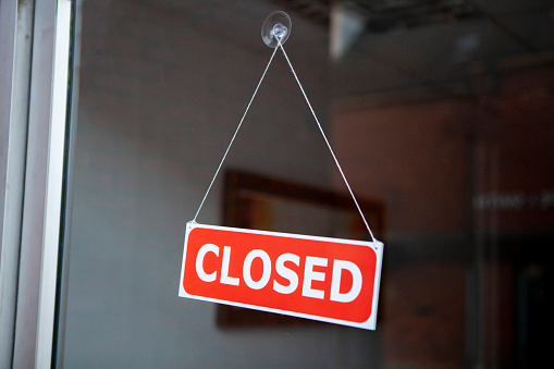 Red sign with 'closed' written in white writing, and hanging by a string on a glass shop door