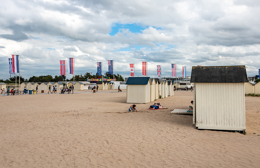 Ouistreham, France. Monday 27 July 2020. People walk by Beach huts and flags in Ouistreham, France