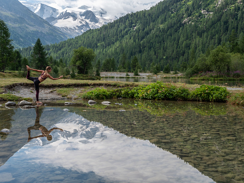 Woman exercising yoga poses by the edge of an alpine lake with glacier view