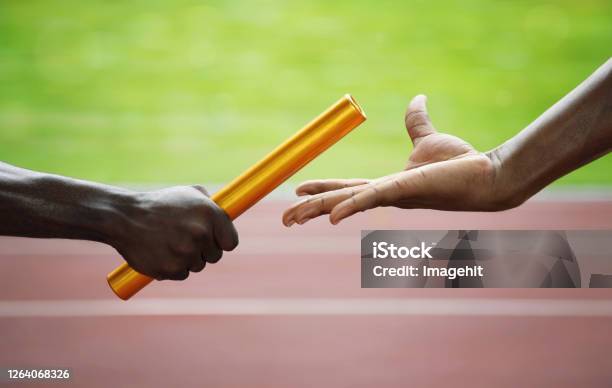 Two Men Passing Golden Baton In Stadium Stock Photo - Download Image Now - Relay Baton, Sport, Adult