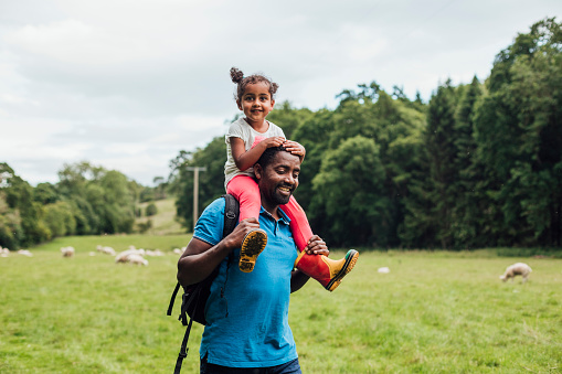 A father carries his young daughter upon his shoulders as they walk through the woods and meadows of Hexham after she gets a little tired from all of the walking.