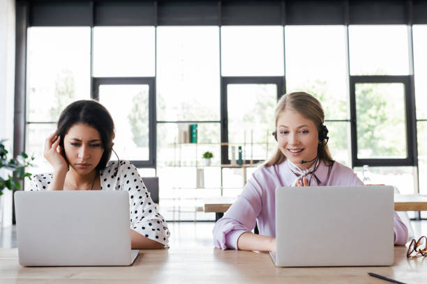 istock happy operator in headset smiling while looking at laptop near coworker 1264072998