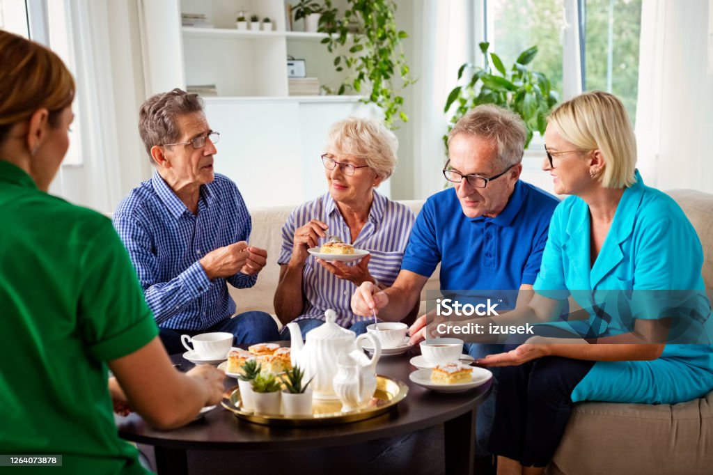 Cheerful senior people in retirement house Happy senior women and man spending time together in nursing home, talking with female social worker and nurse, drinking coffee. 70-79 Years Stock Photo